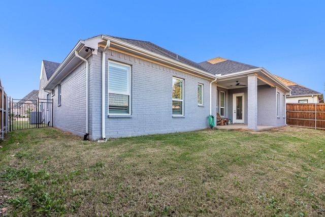 rear view of house with a yard, a fenced backyard, a ceiling fan, and brick siding