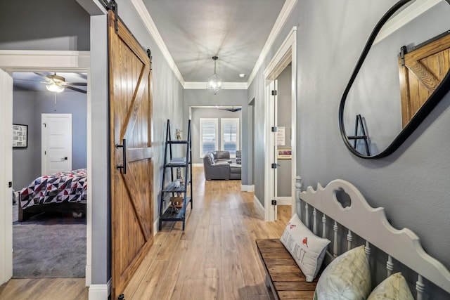 corridor with a barn door, light wood-type flooring, crown molding, and an inviting chandelier