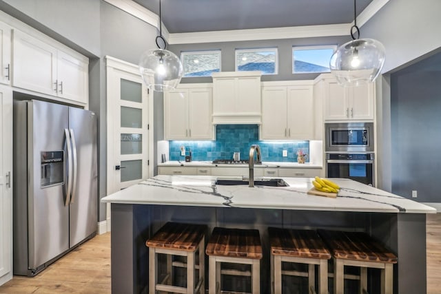 kitchen with light stone counters, backsplash, stainless steel appliances, white cabinetry, and a sink