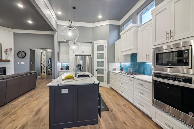 kitchen with a kitchen island with sink, hanging light fixtures, stainless steel appliances, light hardwood / wood-style floors, and white cabinets