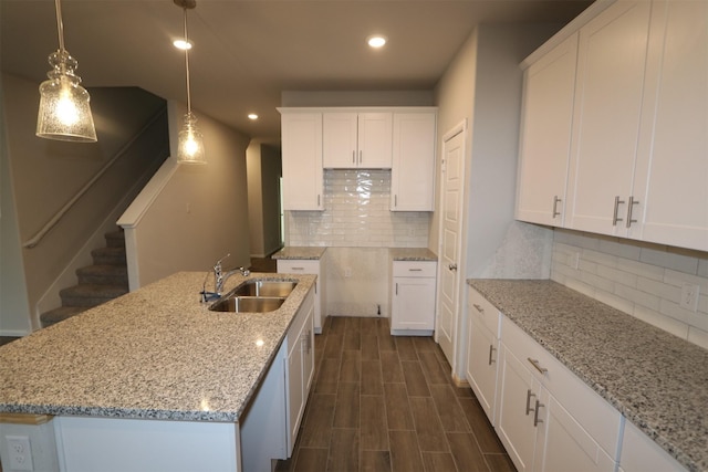 kitchen featuring dark wood-style flooring, a sink, white cabinets, light stone countertops, and decorative light fixtures