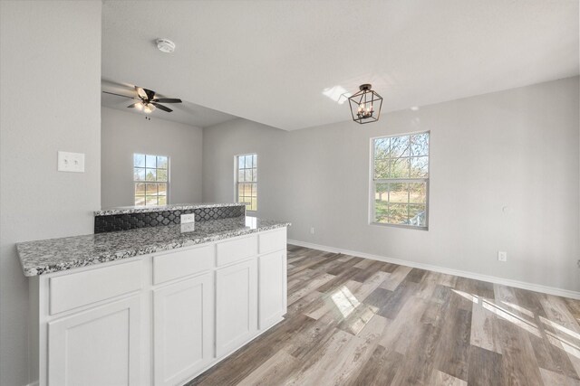 kitchen with light stone countertops, plenty of natural light, white cabinets, and light hardwood / wood-style flooring