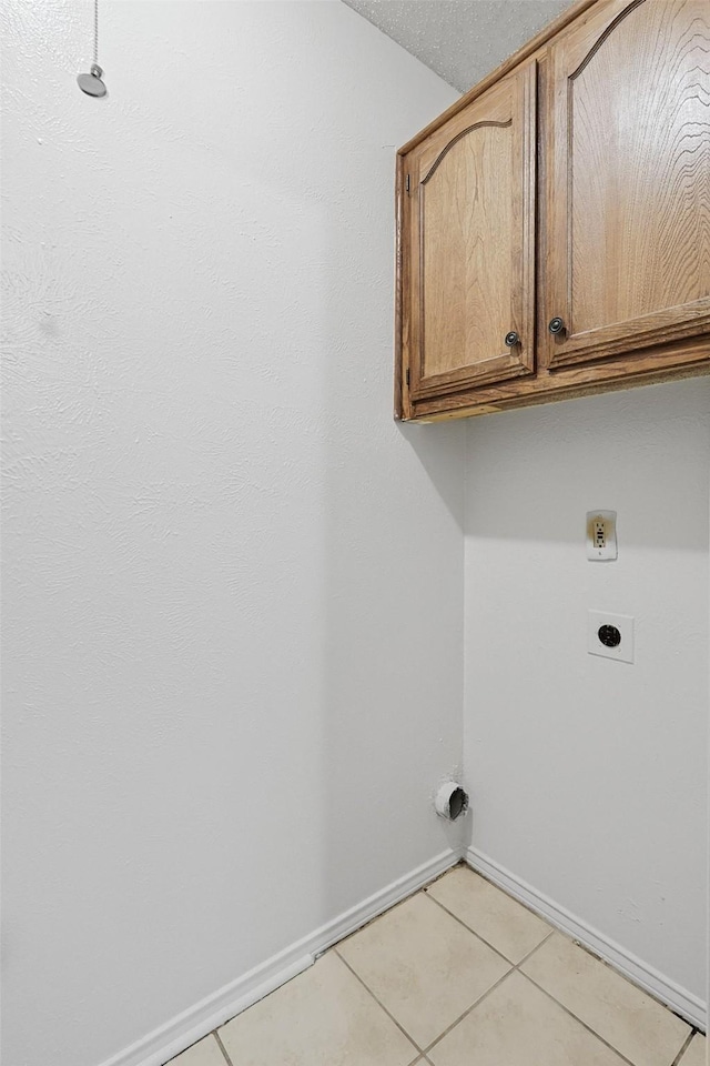 clothes washing area featuring cabinets, electric dryer hookup, and light tile patterned flooring