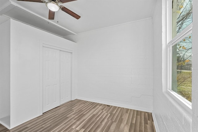 unfurnished bedroom featuring ceiling fan, wood-type flooring, brick wall, and a closet