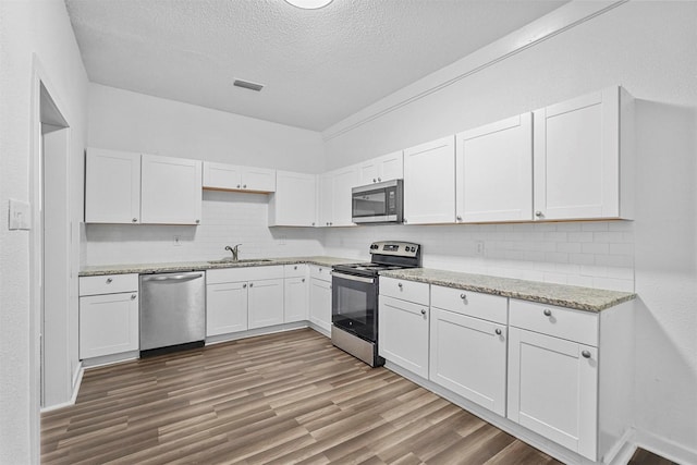 kitchen with sink, stainless steel appliances, backsplash, wood-type flooring, and white cabinets