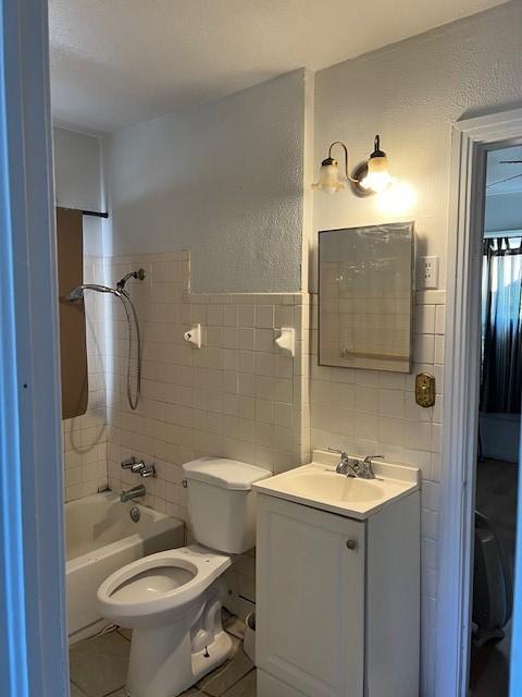 full bathroom featuring vanity, tiled shower / bath combo, tile walls, tile patterned flooring, and toilet