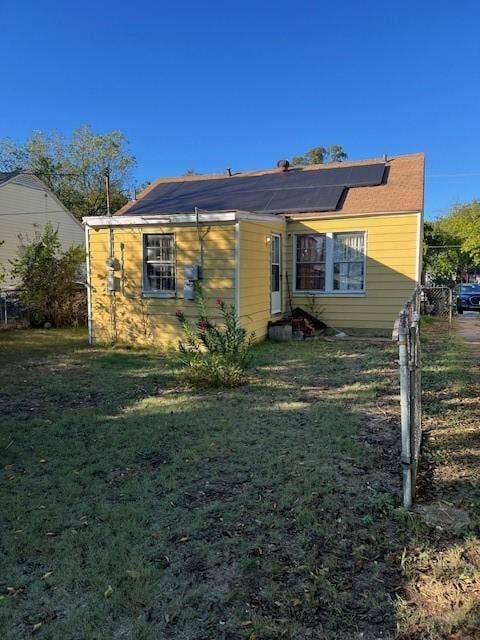 back of house with solar panels and a lawn