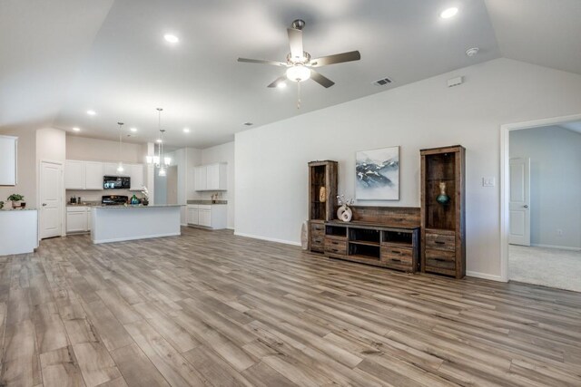 living room with ceiling fan with notable chandelier, light hardwood / wood-style floors, and lofted ceiling