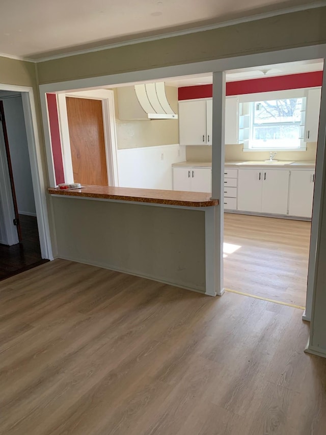 kitchen featuring white cabinets, sink, light hardwood / wood-style floors, kitchen peninsula, and extractor fan