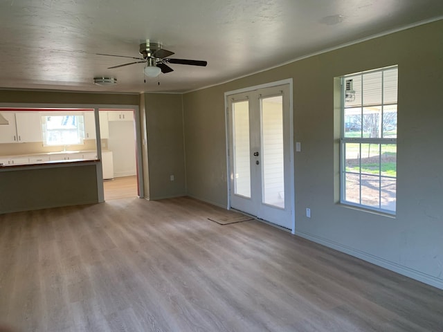 unfurnished living room with ceiling fan, french doors, light hardwood / wood-style floors, and ornamental molding