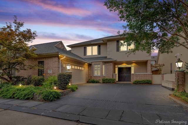 view of front of home with brick siding, driveway, an attached garage, and stucco siding