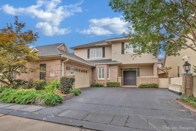 view of front of property featuring a garage, driveway, brick siding, and stucco siding