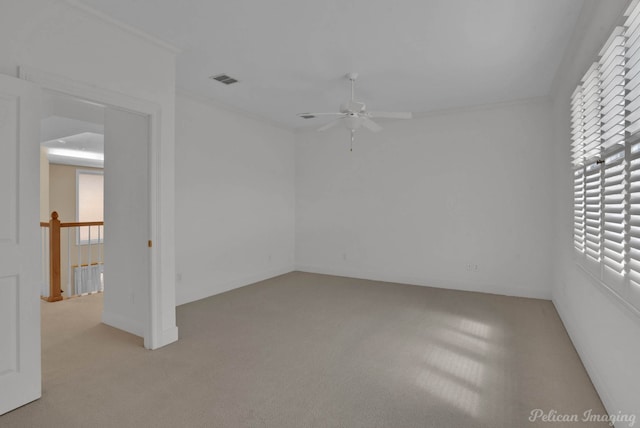 spare room featuring a ceiling fan, visible vents, crown molding, and light colored carpet