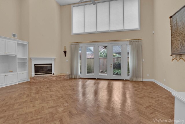 unfurnished living room with light parquet flooring, plenty of natural light, a towering ceiling, and a brick fireplace