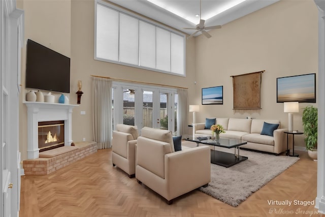 living room with french doors, ceiling fan, a towering ceiling, a fireplace, and light parquet flooring