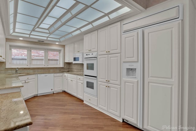 kitchen featuring white appliances, light wood finished floors, light stone counters, white cabinetry, and a sink