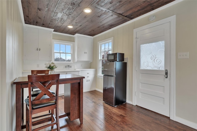 kitchen with dark wood-style flooring, wooden ceiling, freestanding refrigerator, white cabinets, and black microwave