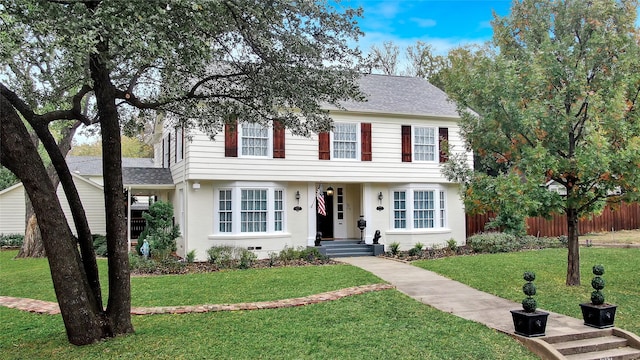 colonial home with a shingled roof, a front yard, and fence