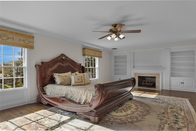 bedroom with wood finished floors, visible vents, a fireplace with flush hearth, a ceiling fan, and crown molding