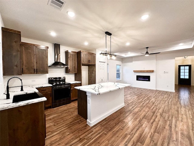 kitchen with a kitchen island, decorative light fixtures, wall chimney range hood, wood-type flooring, and black electric range