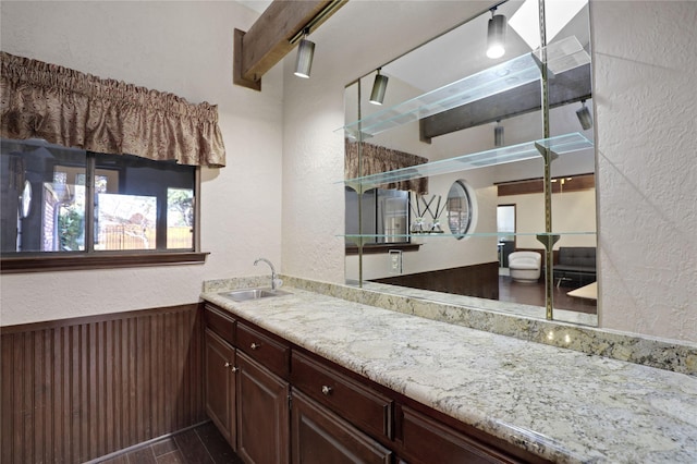 kitchen with light stone counters, sink, and beamed ceiling