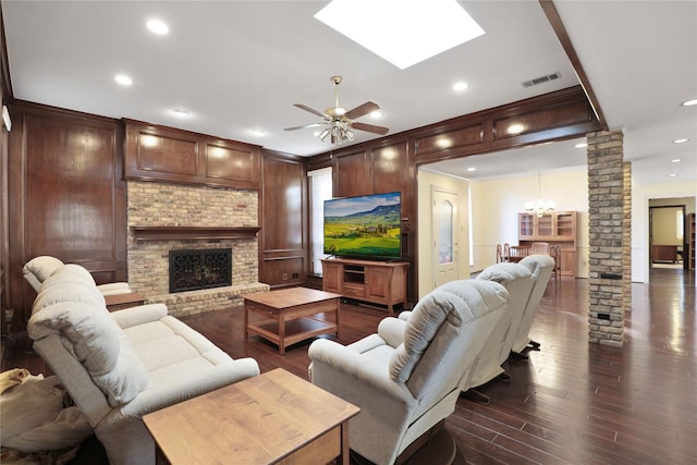 living room with ceiling fan with notable chandelier, dark wood-type flooring, a fireplace, and decorative columns