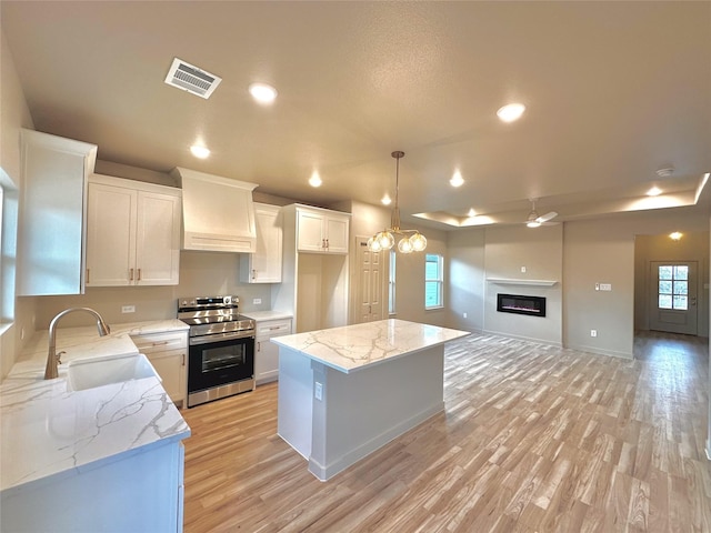 kitchen with electric stove, a kitchen island, custom exhaust hood, sink, and white cabinetry