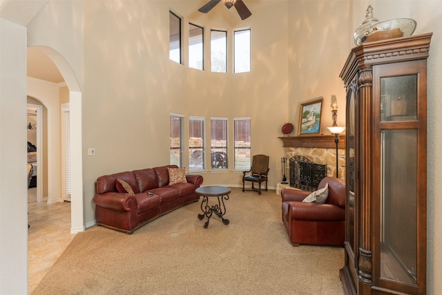 carpeted living room featuring ceiling fan, a fireplace, and a high ceiling