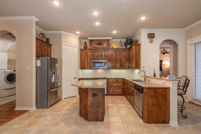 kitchen featuring stainless steel appliances, washer / dryer, a sink, a peninsula, and light stone countertops