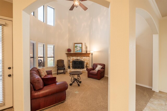 living room featuring a high ceiling, ceiling fan, ornamental molding, a fireplace, and light colored carpet