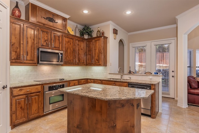 kitchen featuring a sink, stainless steel appliances, arched walkways, a center island, and light stone counters