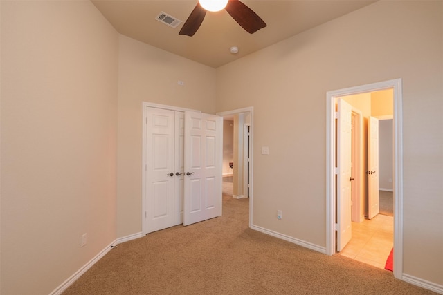 unfurnished bedroom with ceiling fan, light colored carpet, a towering ceiling, and a closet