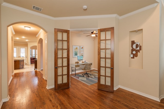 corridor featuring french doors, arched walkways, crown molding, wood finished floors, and a desk