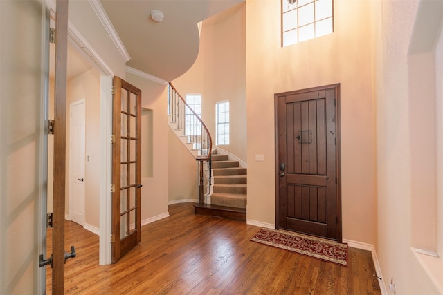 foyer featuring wood-type flooring, ornamental molding, a high ceiling, and french doors