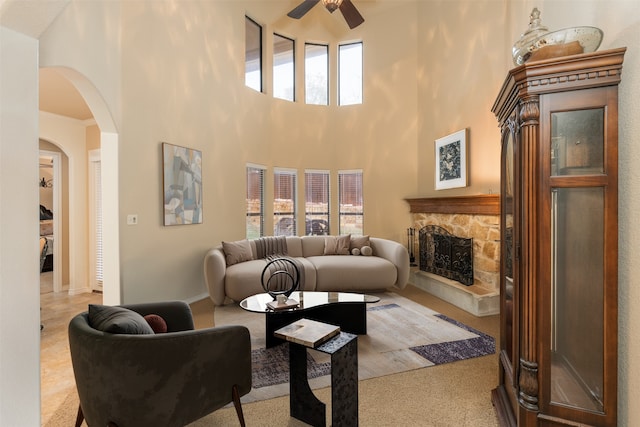 living area with ceiling fan, plenty of natural light, arched walkways, a stone fireplace, and a towering ceiling