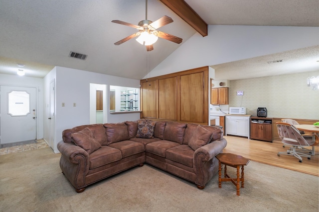 living room with vaulted ceiling with beams, ceiling fan, light hardwood / wood-style flooring, and a textured ceiling