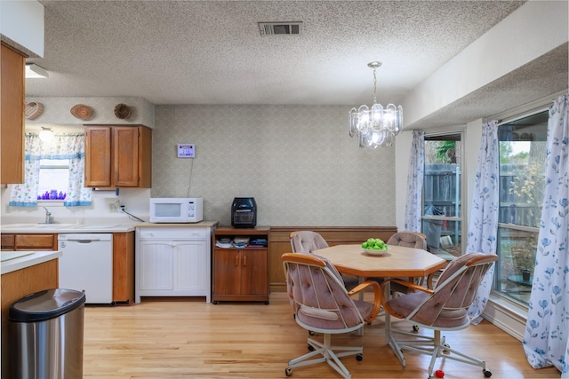 kitchen with an inviting chandelier, pendant lighting, white appliances, and light hardwood / wood-style floors