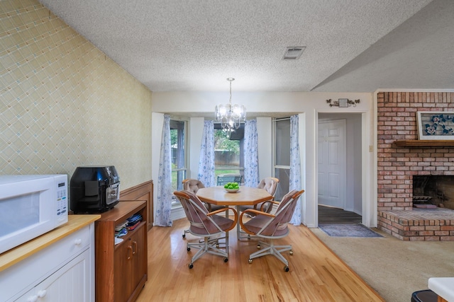 dining space featuring a fireplace, light hardwood / wood-style floors, a textured ceiling, and a notable chandelier