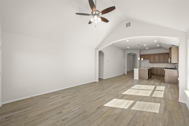 unfurnished living room with sink, vaulted ceiling, ceiling fan, and light wood-type flooring