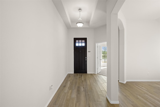 entryway with a tray ceiling, light hardwood / wood-style flooring, and a towering ceiling