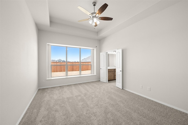 unfurnished bedroom with a raised ceiling, connected bathroom, light colored carpet, and ceiling fan