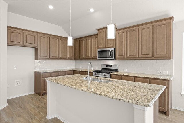 kitchen featuring light stone counters, stainless steel appliances, a kitchen island with sink, sink, and hardwood / wood-style floors