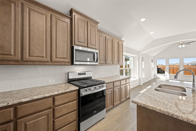 kitchen with lofted ceiling, sink, light stone counters, appliances with stainless steel finishes, and decorative backsplash