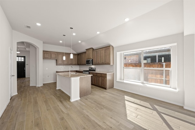 kitchen with decorative light fixtures, vaulted ceiling, an island with sink, stainless steel appliances, and light stone countertops