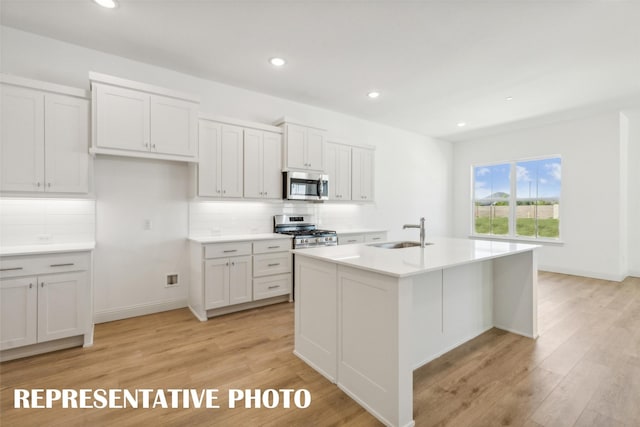 kitchen with sink, light hardwood / wood-style flooring, decorative backsplash, an island with sink, and stainless steel appliances