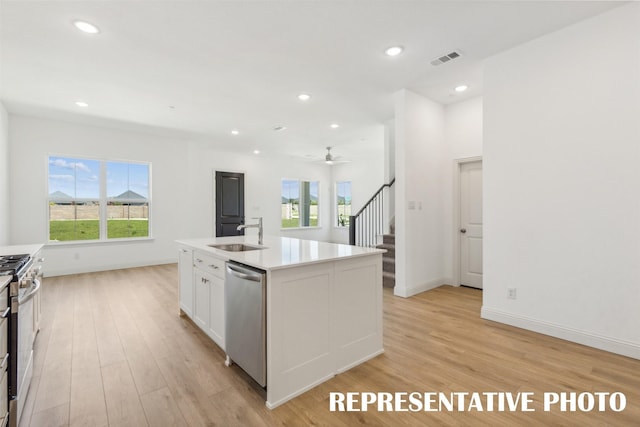 kitchen featuring appliances with stainless steel finishes, sink, light hardwood / wood-style flooring, white cabinets, and an island with sink