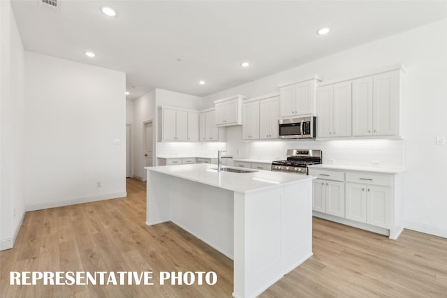 kitchen with light wood-type flooring, stainless steel appliances, sink, white cabinets, and an island with sink