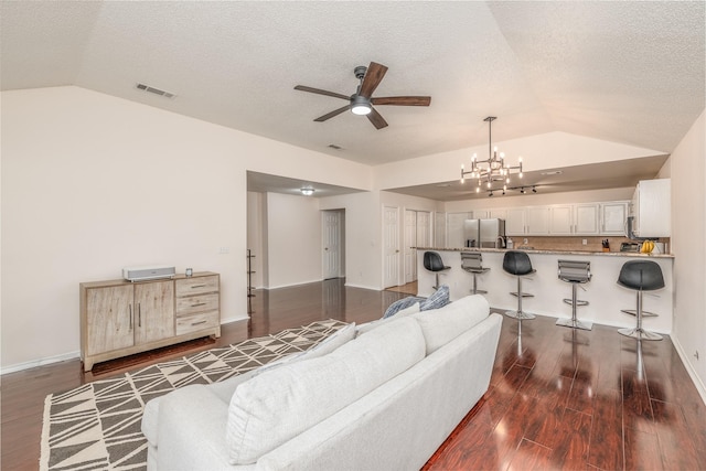 living room with dark hardwood / wood-style flooring, ceiling fan with notable chandelier, a textured ceiling, and lofted ceiling