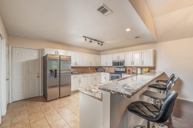 kitchen with kitchen peninsula, light stone countertops, stainless steel appliances, white cabinetry, and a breakfast bar area