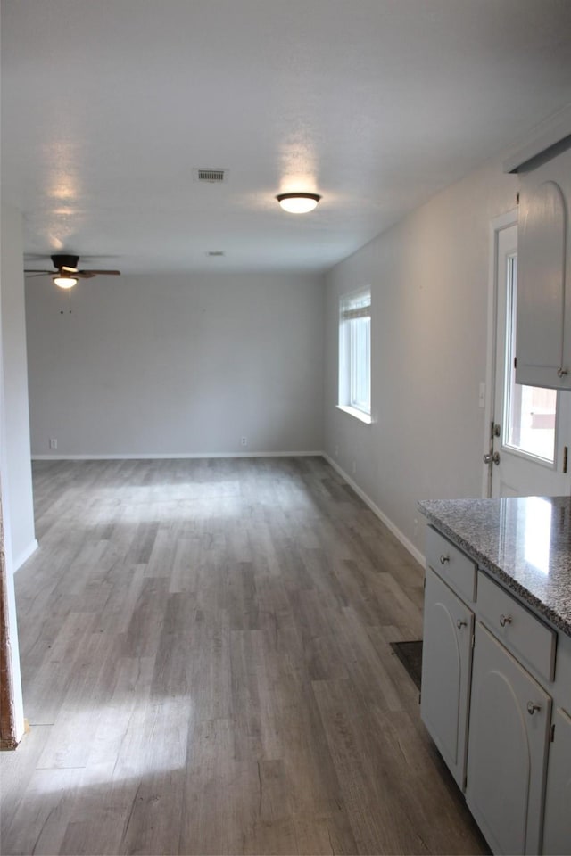 interior space featuring white cabinets, ceiling fan, light stone counters, and light wood-type flooring